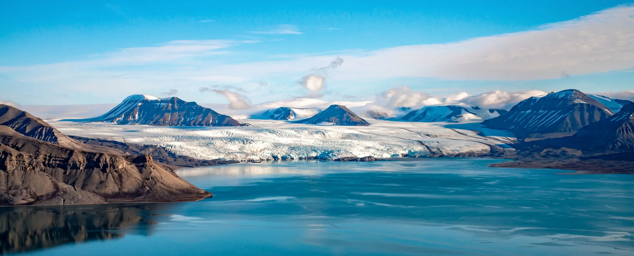 Panoramic tidewater glacier front across a calm summer fjord
