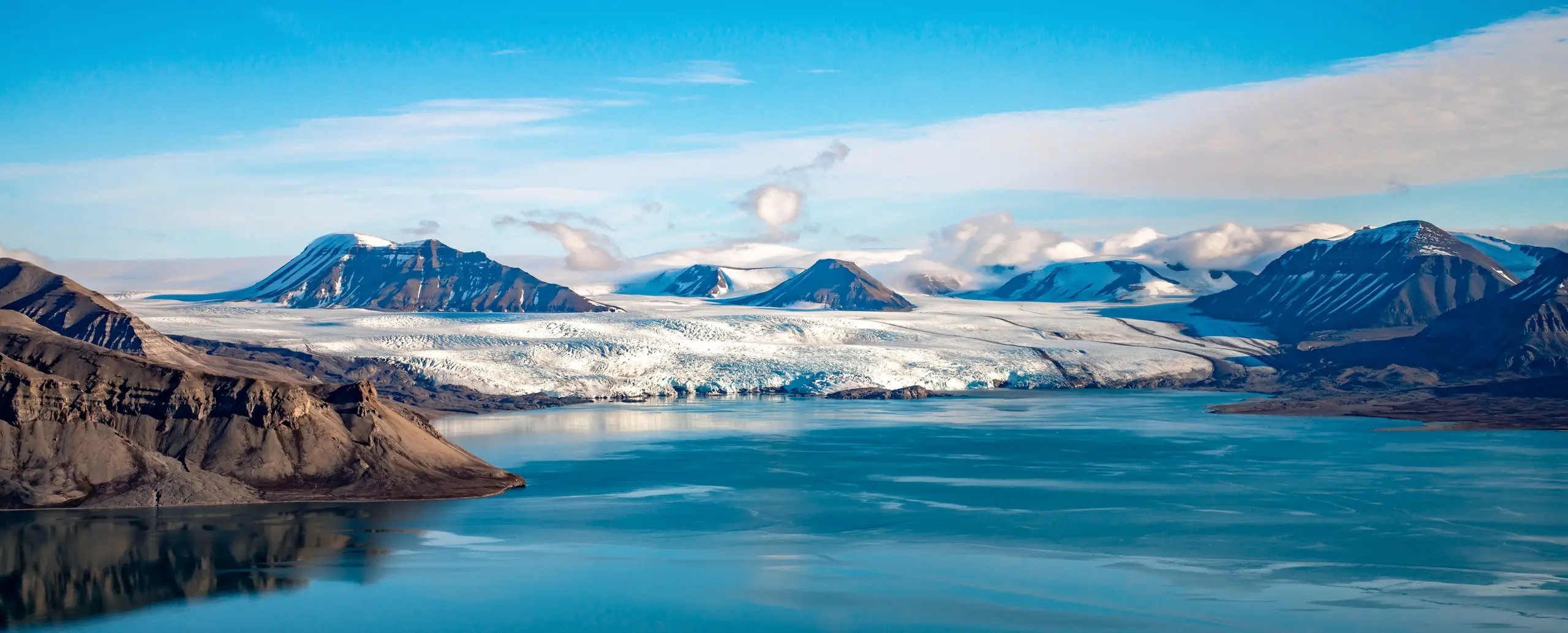 Panoramic tidewater glacier front across a calm summer fjord
