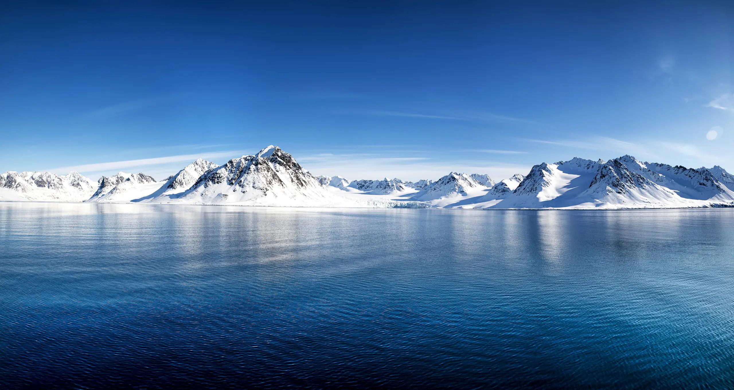 Snow peaks mirrored in a deep-blue Svalbard fjord