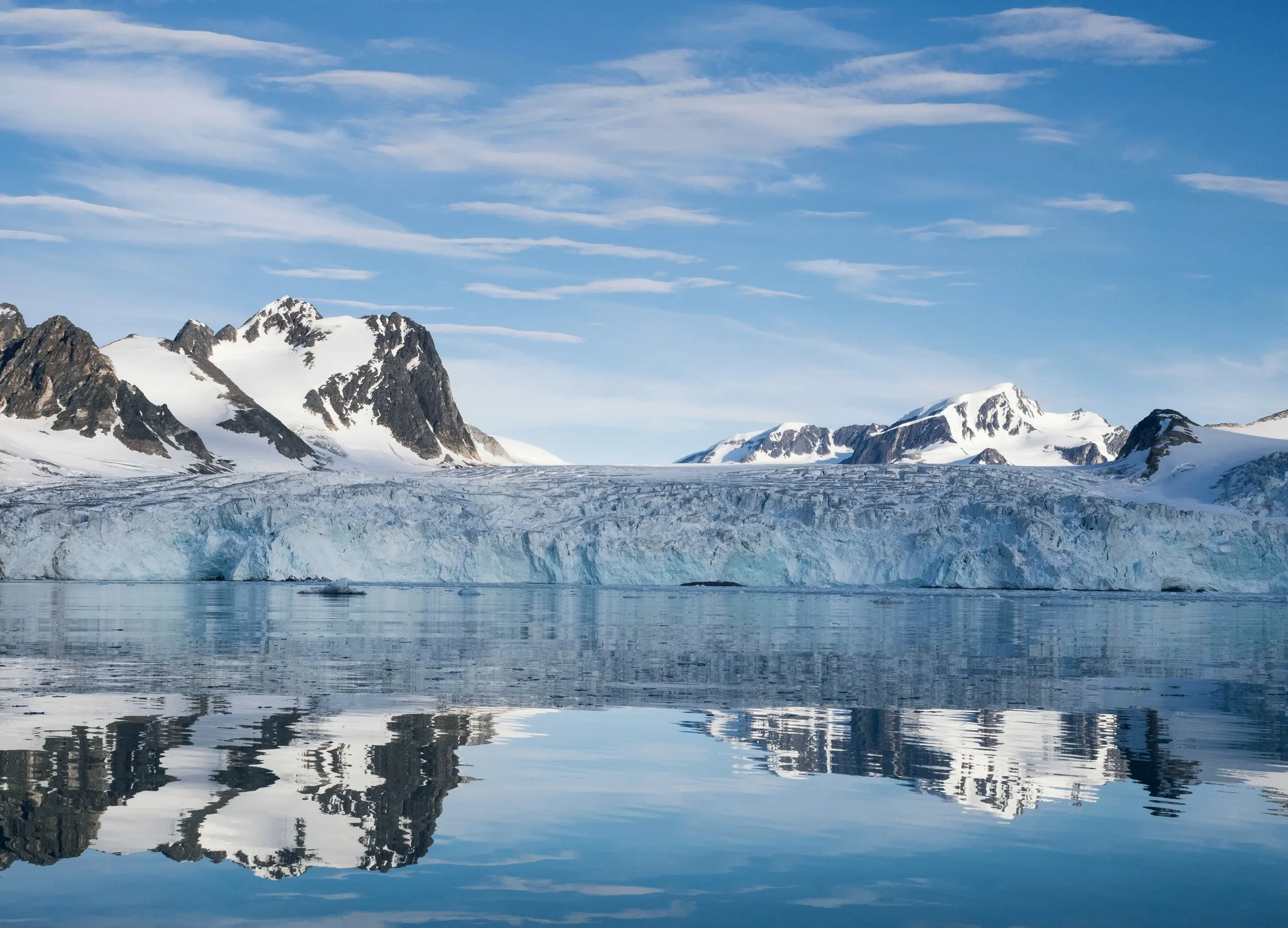 Glacier front and peaks reflected in calm Arctic water