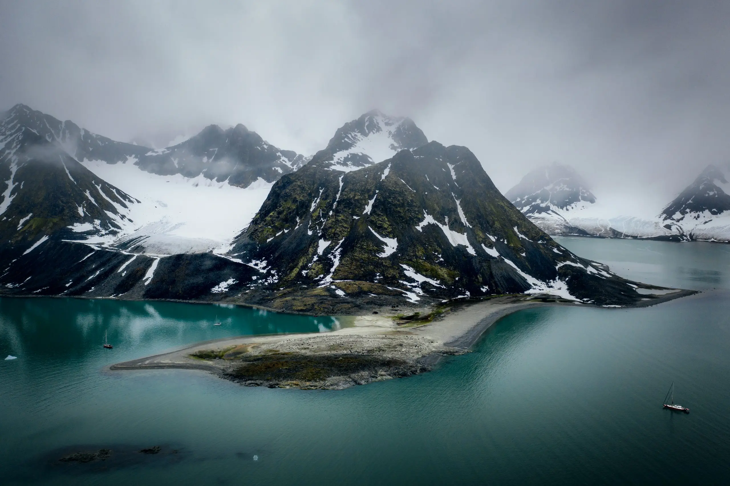 Moody open-ocean fjord with snow peaks and a lone sailboat