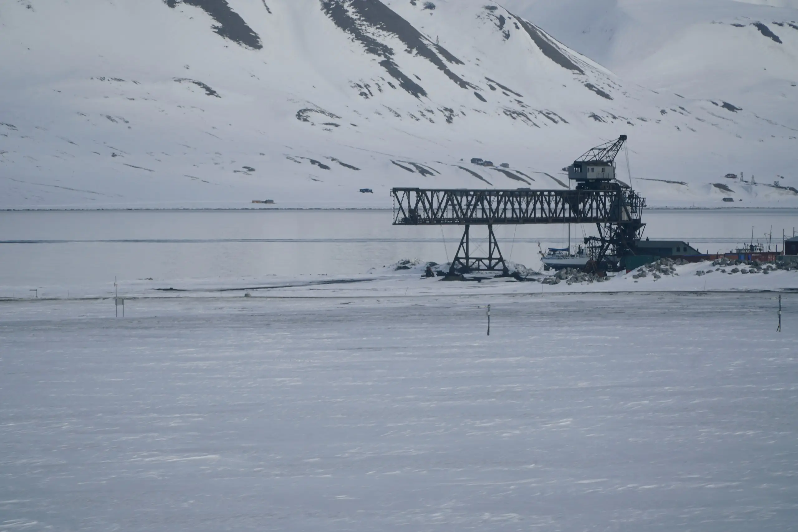 A disused coal-loading crane on a frozen Svalbard fjord below snowy mountains