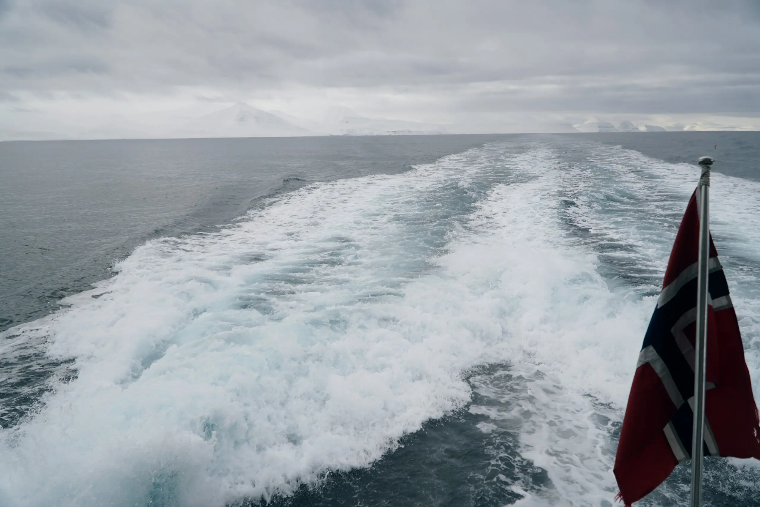 Ship's wake and Norwegian flag over open water on the northbound passage