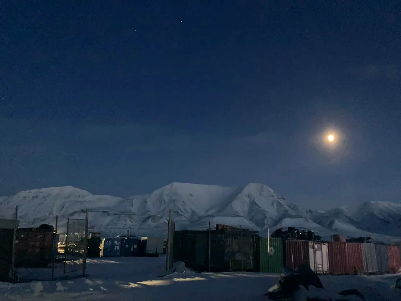 Moonrise over snowy peaks beyond the Longyearbyen harbor in winter