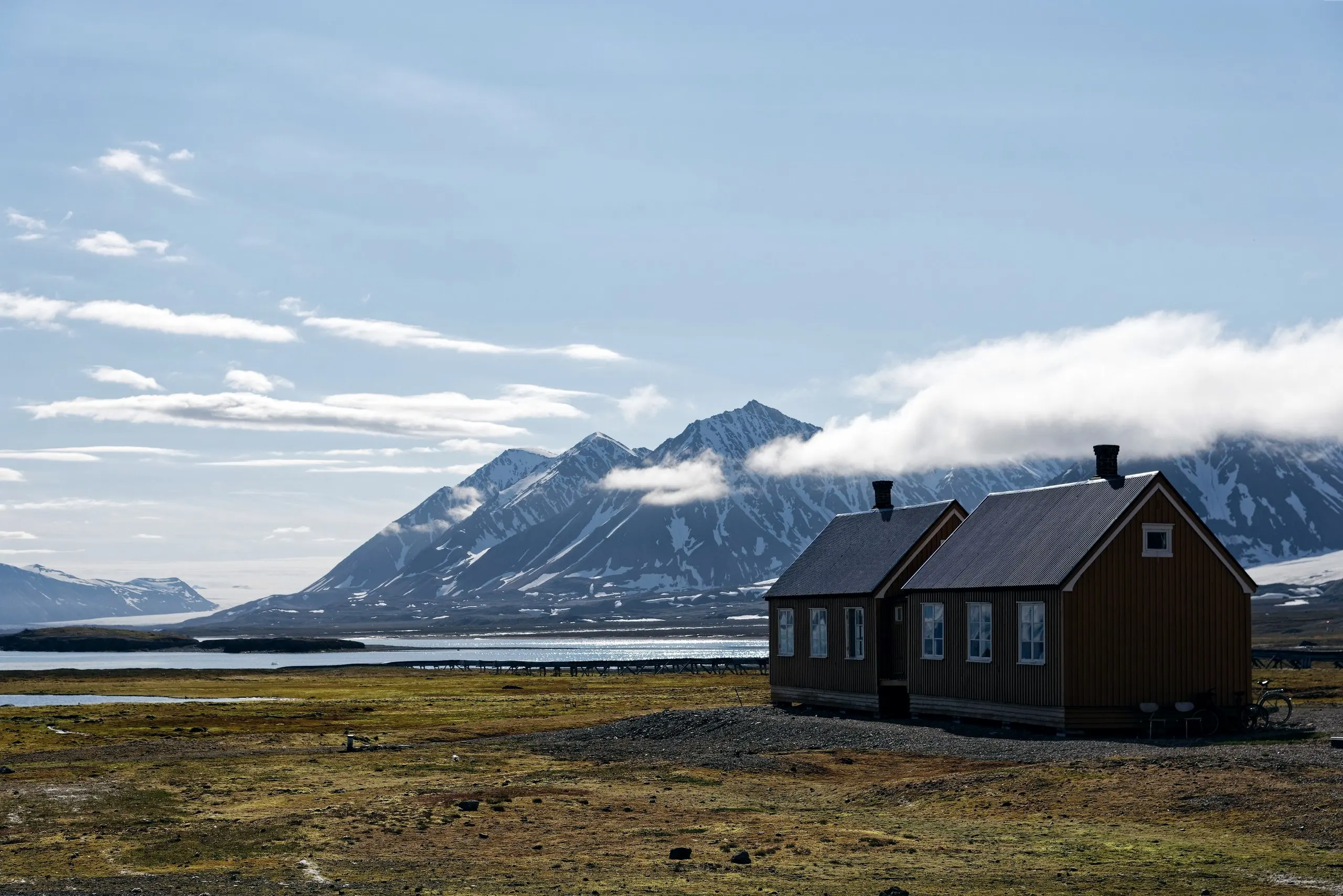 Arctic cottage by a fjord below snow-streaked peaks in summer