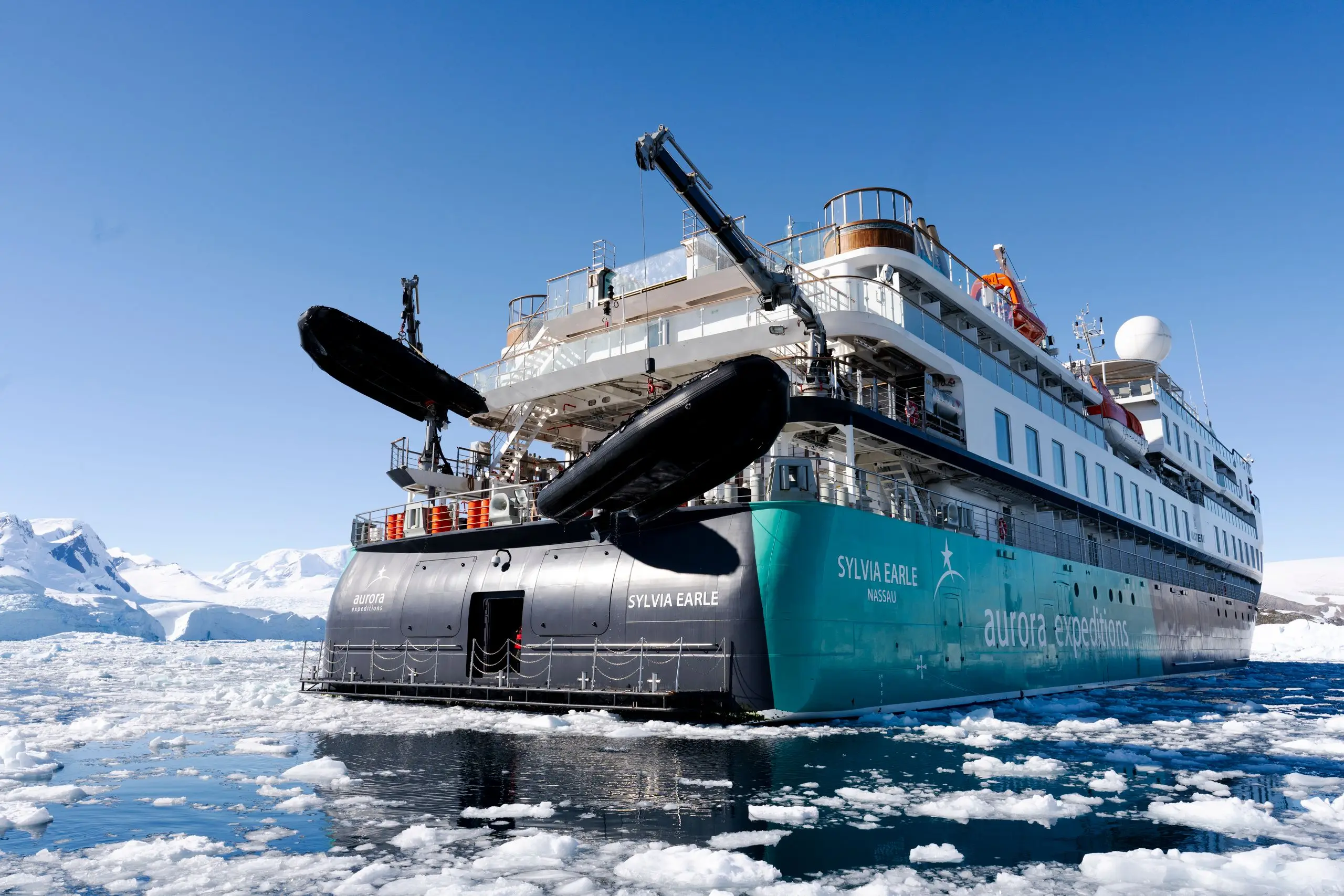 A modern expedition cruise ship among the sea ice below snowy Arctic peaks