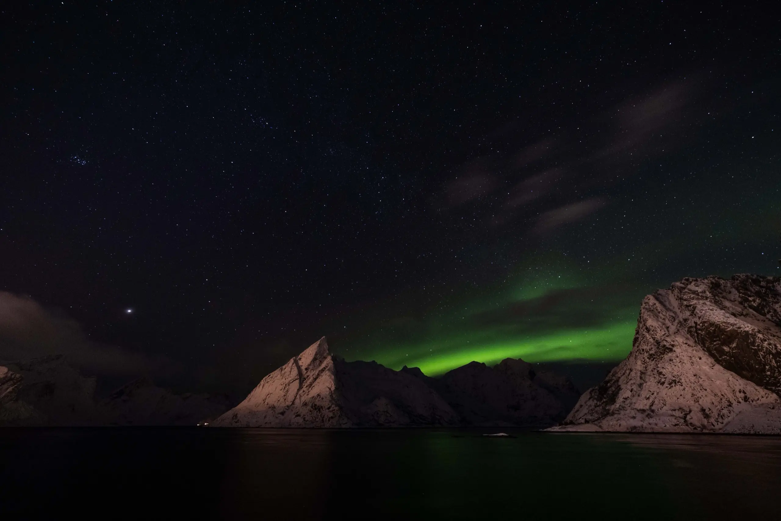 Green aurora over snow-covered peaks above a dark fjord at night